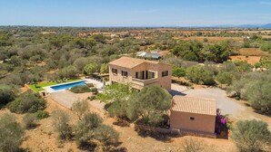 A stone villa with a swimming pool, surrounded by trees and a view of distant hills.