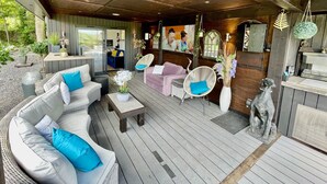 Un espacio de estar al aire libre techado con mobiliario de mimbre, una terraza de madera y una estatua de piedra.