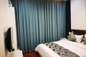 Quarto de hotel com cama, cortinas, televisão e mesa de cabeceira.
