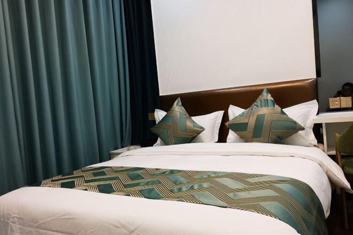 A bed with a patterned bedspread, pillows with geometric designs, and a dark curtain.