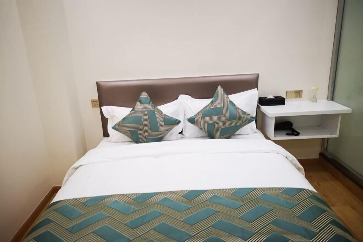 A neatly made bed with a patterned bedspread, two decorative pillows, and a bedside table with a lamp and a small box.