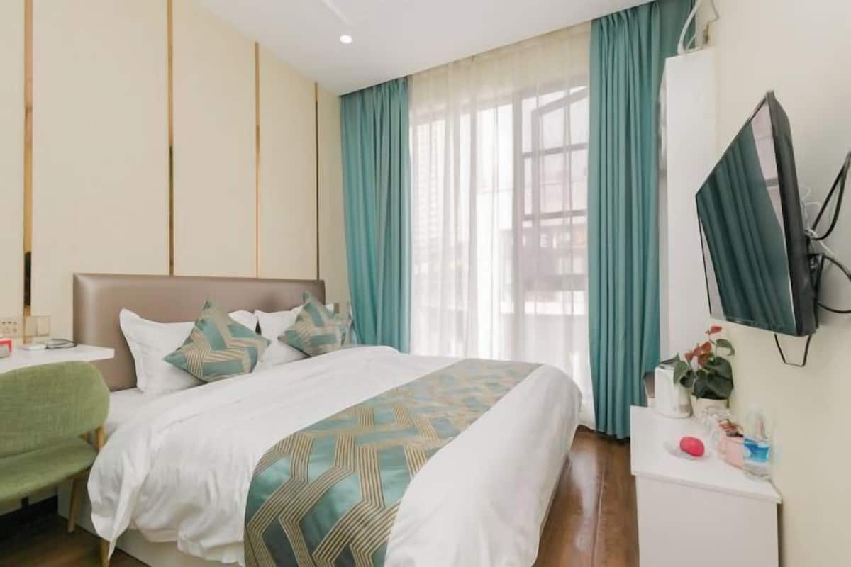 Une chambre d’hôtel avec un lit, un bureau, une chaise, une télévision et une fenêtre avec des rideaux.