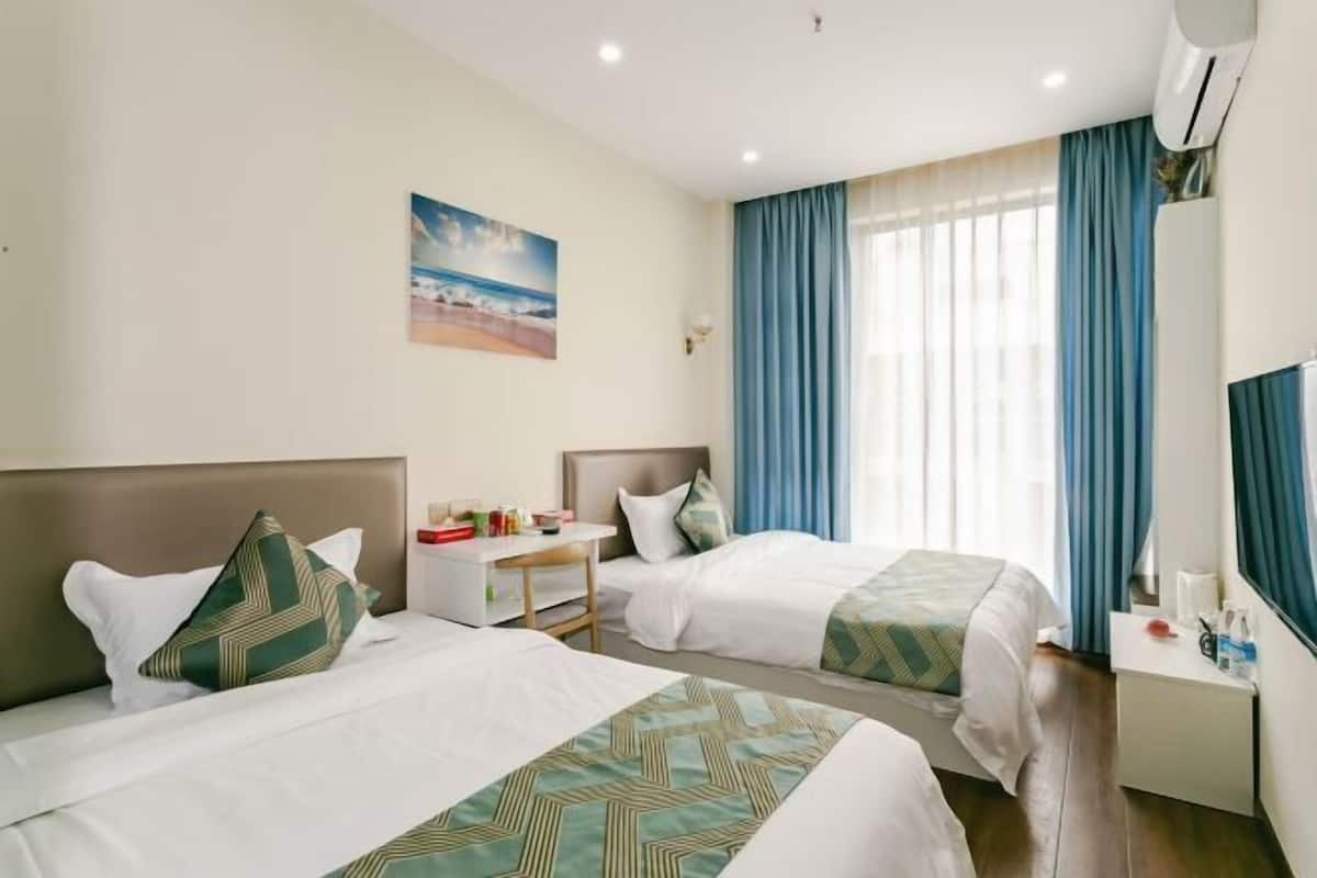 Une chambre d’hôtel avec deux lits, un bureau, une chaise, une télévision et une fenêtre avec des rideaux.