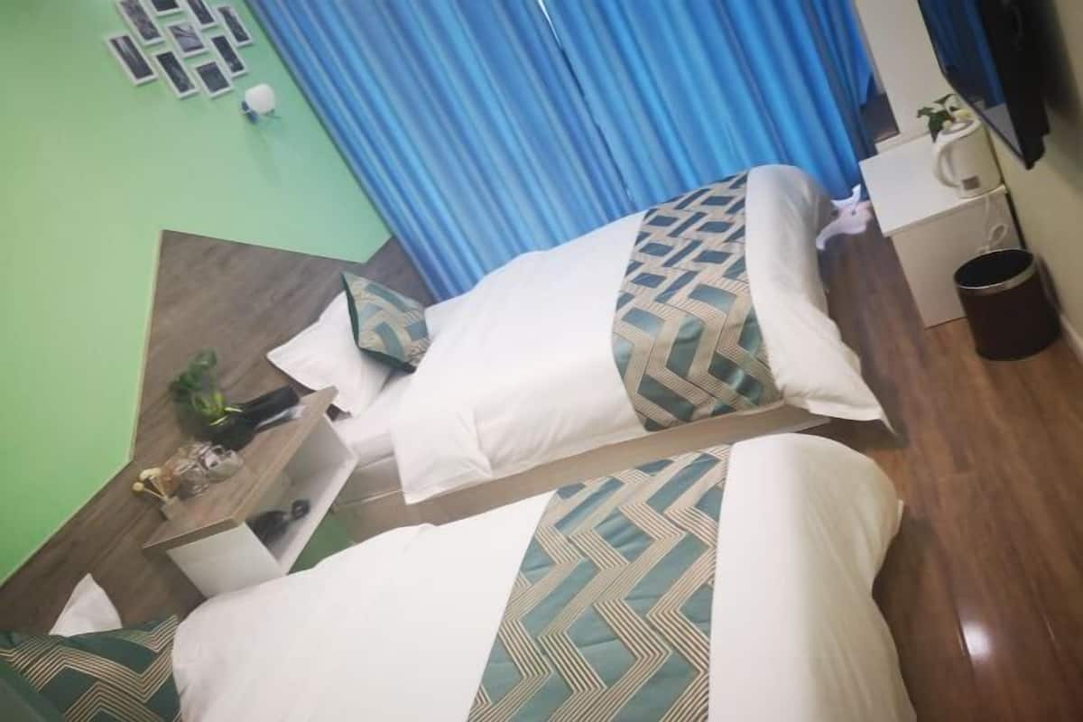 Une chambre d’hôtel avec deux lits, une table de chevet en bois, une petite table et un rideau bleu.