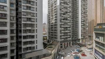 A high-rise residential building with multiple balconies, a parking lot with several cars, and a commercial building with signage.