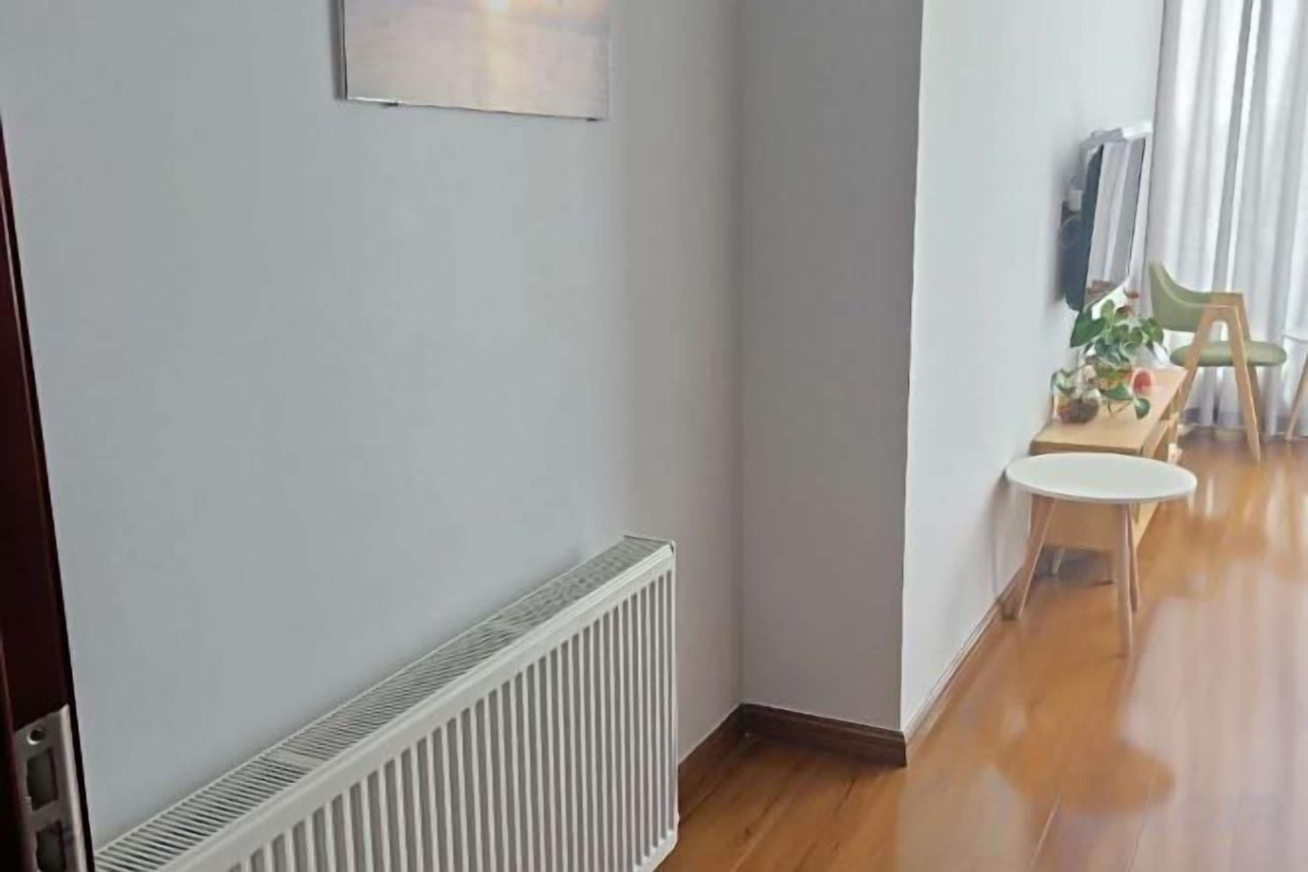 A hallway with a radiator, a small table with a chair, and a window with curtains.