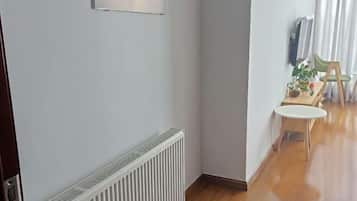 A hallway with a radiator, a small table with a chair, and a window with curtains.