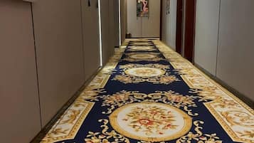 A hallway with a patterned carpet, doors on either side, and artwork on the walls.