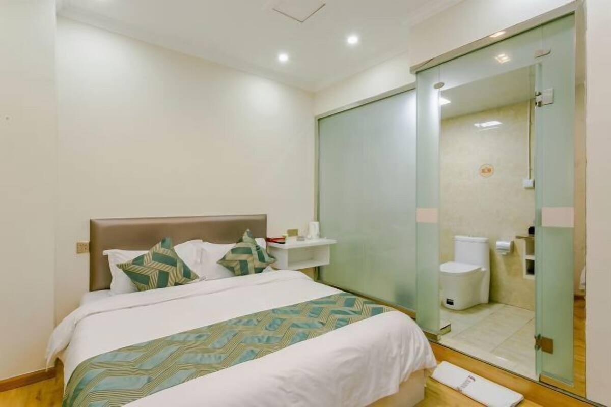 Une chambre d’hôtel comprenant un lit, une table de chevet, une cabine de douche en verre et des toilettes.