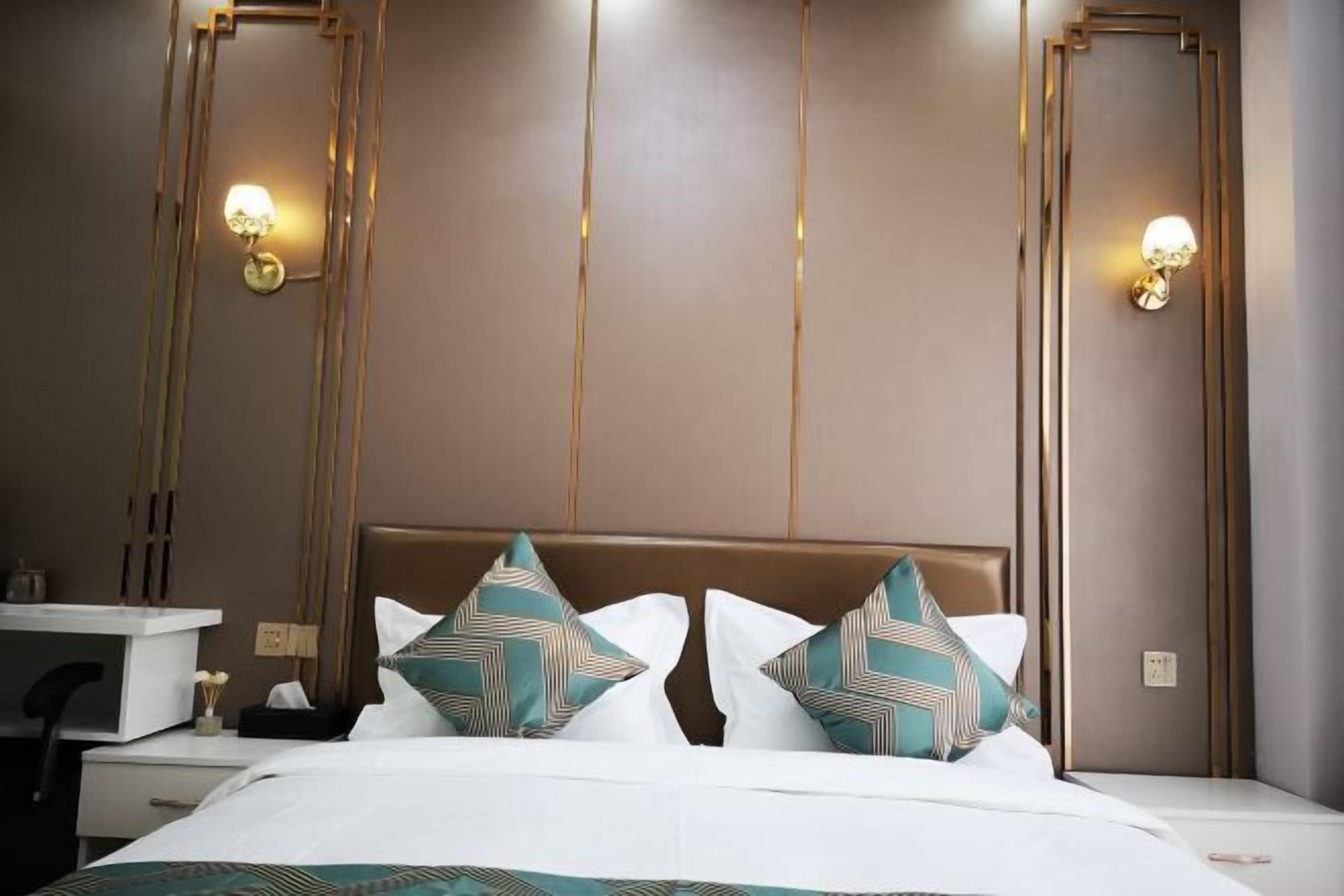A hotel room with a bed, bedside tables, and wall-mounted lamps.