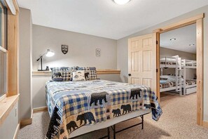 Un dormitorio con una cama, una mesita de noche, una lámpara, un reloj de pared, una puerta y una cama individual al fondo.