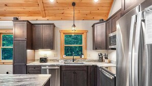 Una cucina moderna con mobili scuri, elettrodomestici in acciaio inossidabile, soffitto in legno e una finestra vista alberi.