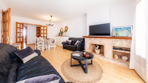 Un salon comprenant un canapé noir, une table basse, une cheminée, un téléviseur et un coin repas avec des chaises et une table.