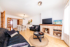 Una sala de estar con un sofá negro, una mesa de centro, una chimenea, un televisor y un comedor con sillas y una mesa.