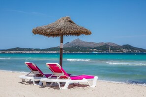 Ein Strand mit zwei weißen Liegestühlen und einem Strohdachschirm.