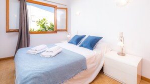 Un lit bien fait, avec une literie bleue et blanche, une lampe de chevet et une fenêtre avec des rideaux.
