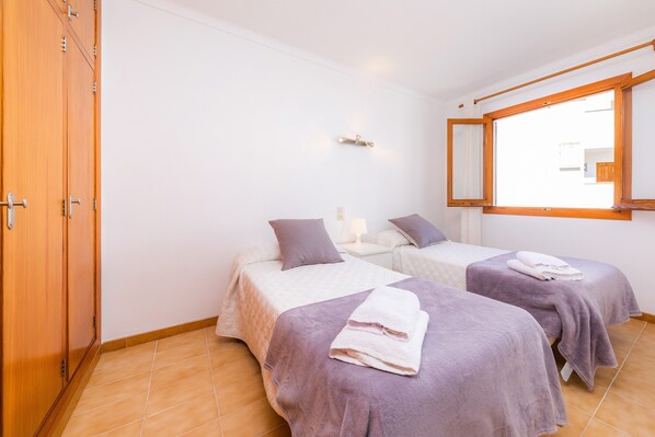 A bedroom with two beds, a wardrobe, a window, and a mirror.