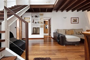 Una sala de estar moderna con una escalera de madera, un conjunto de sofá y una estantería con cuadros enmarcados.