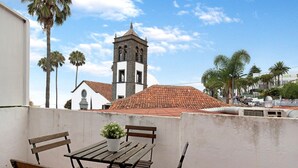 Une terrasse avec une table et des bancs en bois, un pot de fleurs et une vue sur une église dotée d’un clocher.