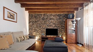 Un salon avec un mur en pierre, un canapé, un pouf, un téléviseur et une lampe.