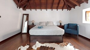 Une chambre avec un plafond en bois, un lit avec une literie à motifs, une chaise bleue et un miroir.