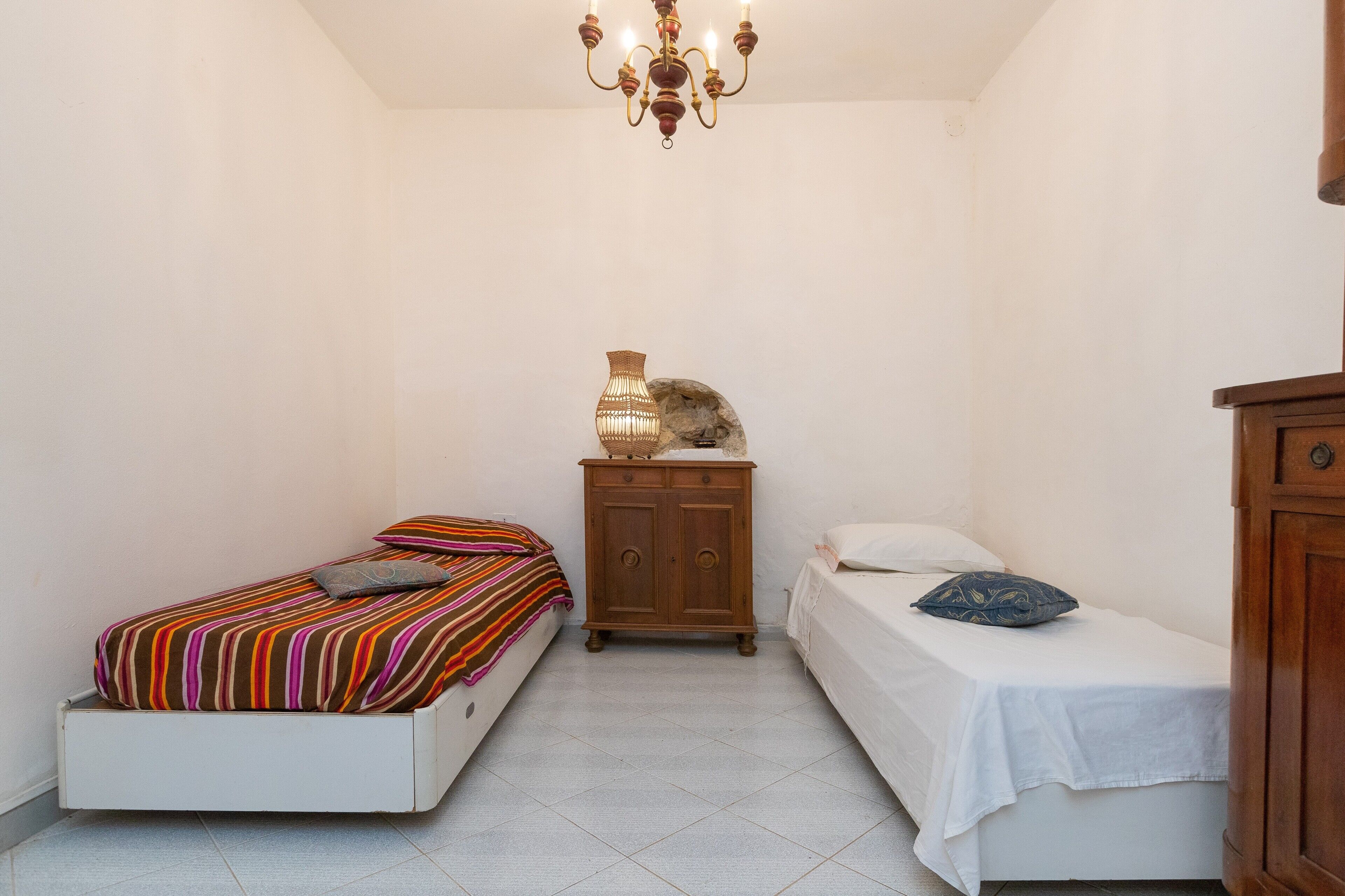 Una camera da letto con due letti, un armadietto in legno, un lampadario e un pavimento piastrellato.