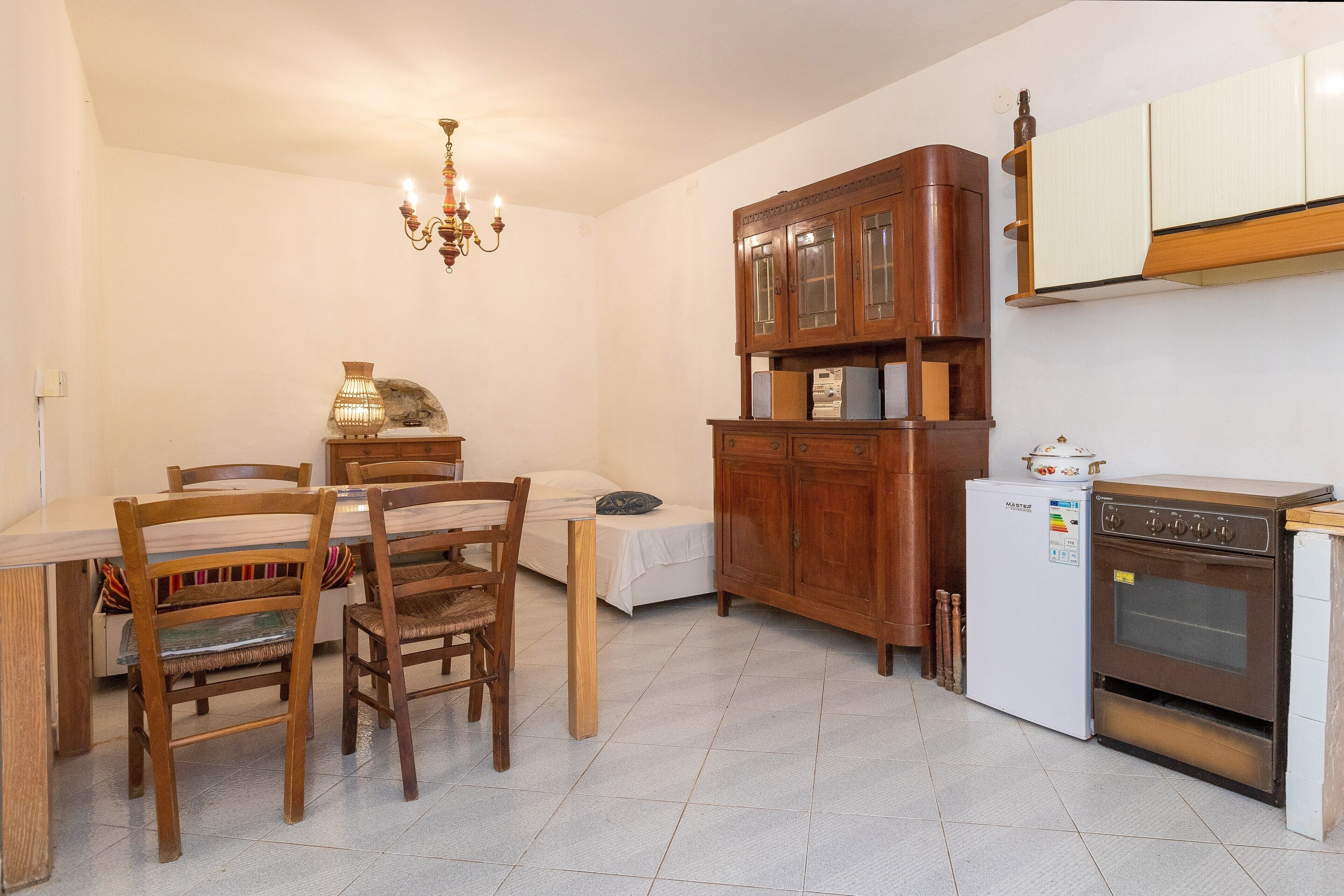 A kitchen with a dining table, chairs, a refrigerator, an oven, and a wooden cabinet.