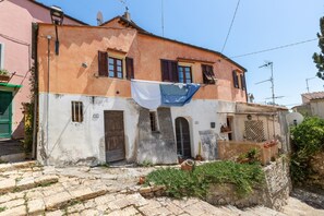 Un bâtiment à deux étages, doté d’une façade en pierre, d’une porte en bois et d’un petit jardin agrémenté de plantes en pot.