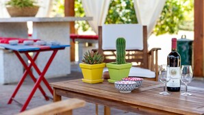 A wooden table with a bottle of wine and two glasses, a yellow and a green potted plant, and a patterned bowl. - Holiday Home 'La Casa di Valverde' with Garden & A/C (Alghero)