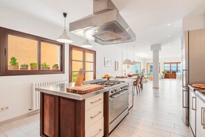 Cocina moderna con isla central, electrodomésticos de acero inoxidable, iluminación colgante y vistas al exterior.