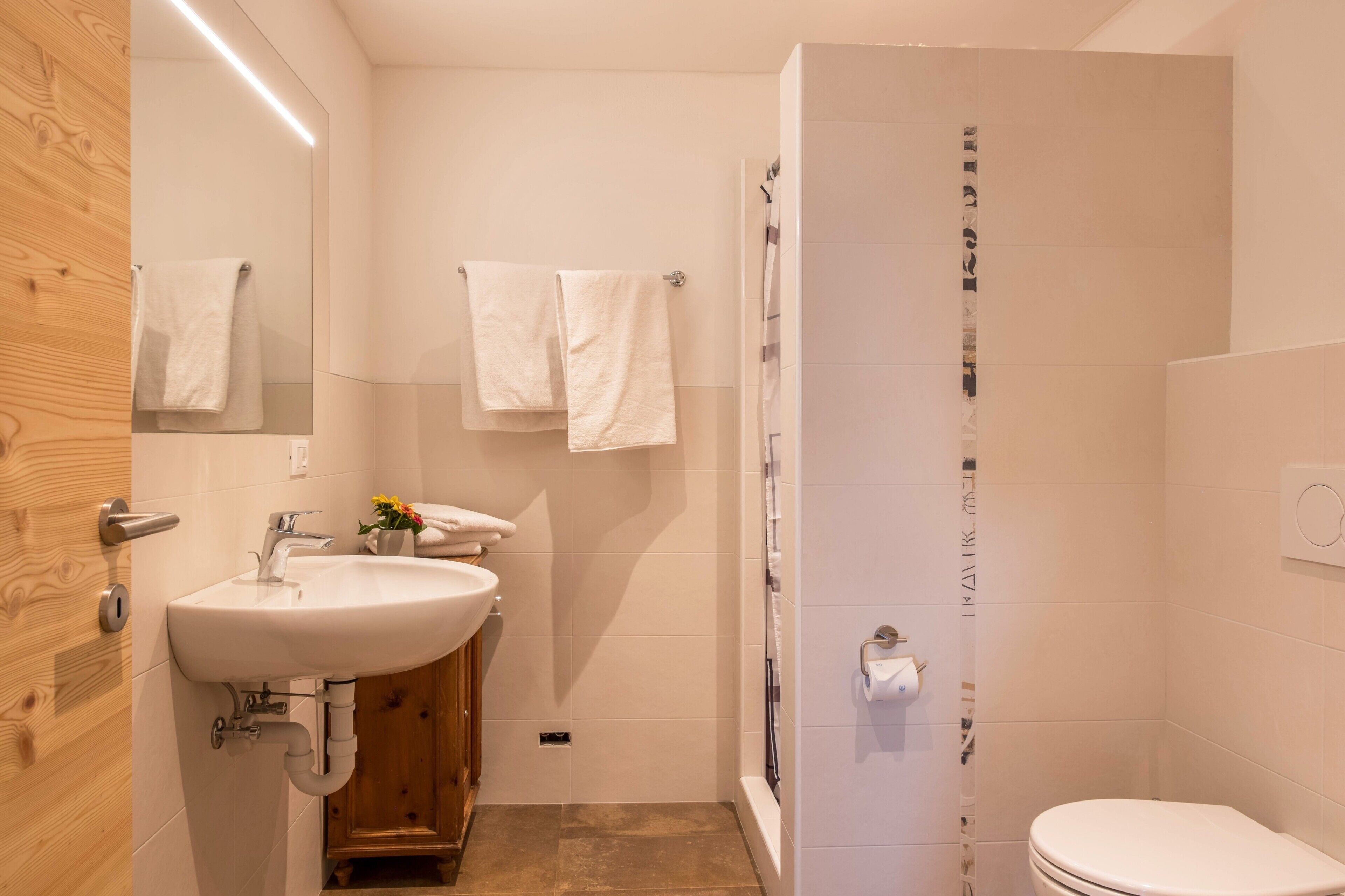 Une salle de bain moderne équipée d’un lavabo, d’un miroir, d’un porte-serviettes, d’une douche et de toilettes.