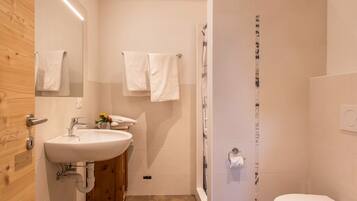 Une salle de bain moderne équipée d’un lavabo, d’un miroir, d’un porte-serviettes, d’une douche et de toilettes.