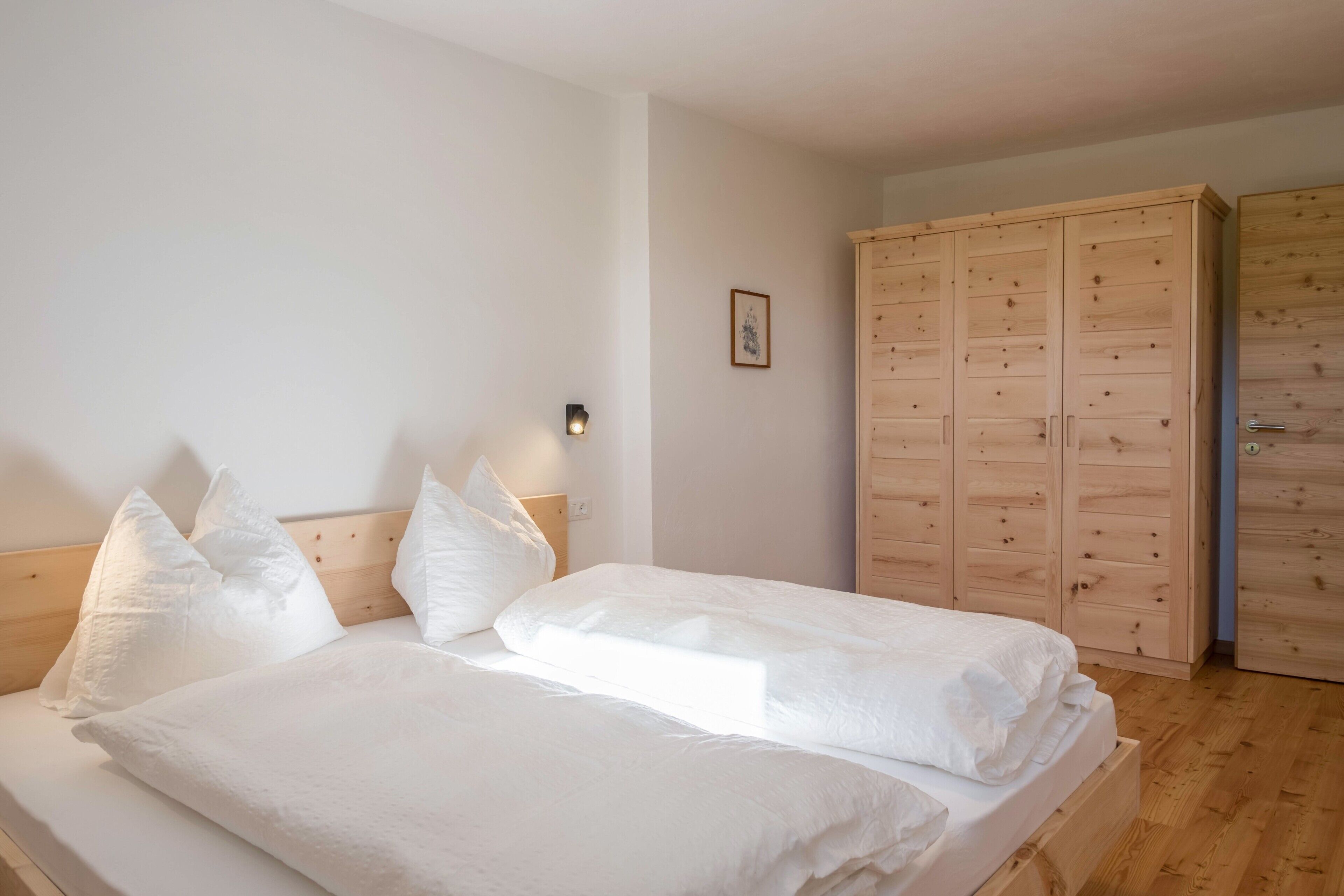 A bedroom with two beds, wooden wardrobe, and a nightstand with a lamp.
