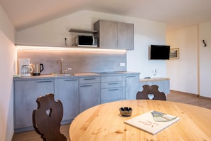 A modern kitchen with grey cabinets, a microwave, a coffee maker, and a dining table with a book.
