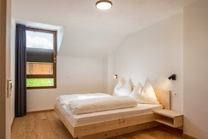 A bedroom with a wooden bed, a window with curtains, a bedside table, and a wall-mounted light.