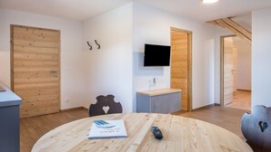 A modern room with a round wooden table, a flat-screen TV mounted on the wall, and wooden doors. - Holiday Apartment 'Nigglhof Katarina' with Mountain View, Balcony & Wi-Fi (redagno)