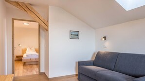 A room with a grey sofa, a bed with white bedding, a framed picture on the wall, and a skylight. - Holiday Apartment 'Nigglhof Katarina' with Mountain View, Balcony & Wi-Fi (redagno)