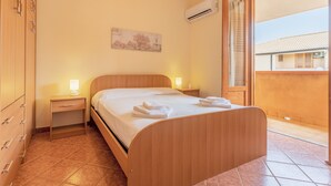 A bedroom with a wooden bed, two bedside tables with lamps, a wall-mounted air conditioner, and a view of the outside. - San Carlo Holiday Home near the Beach with Balcony (Campofelice di Roccella)