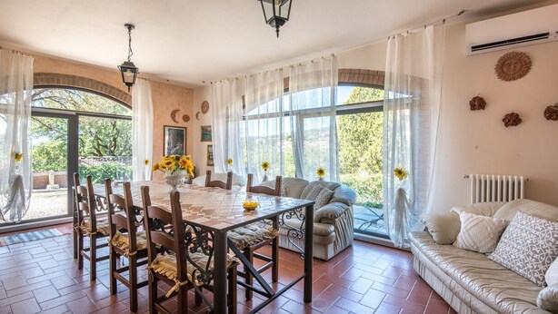 A dining area with a table and chairs, a sofa, and large windows with curtains. - 'Casa Vacanze Chianti Summer' with Pool, Garden & Wi-Fi (Gaiole in Chianti)