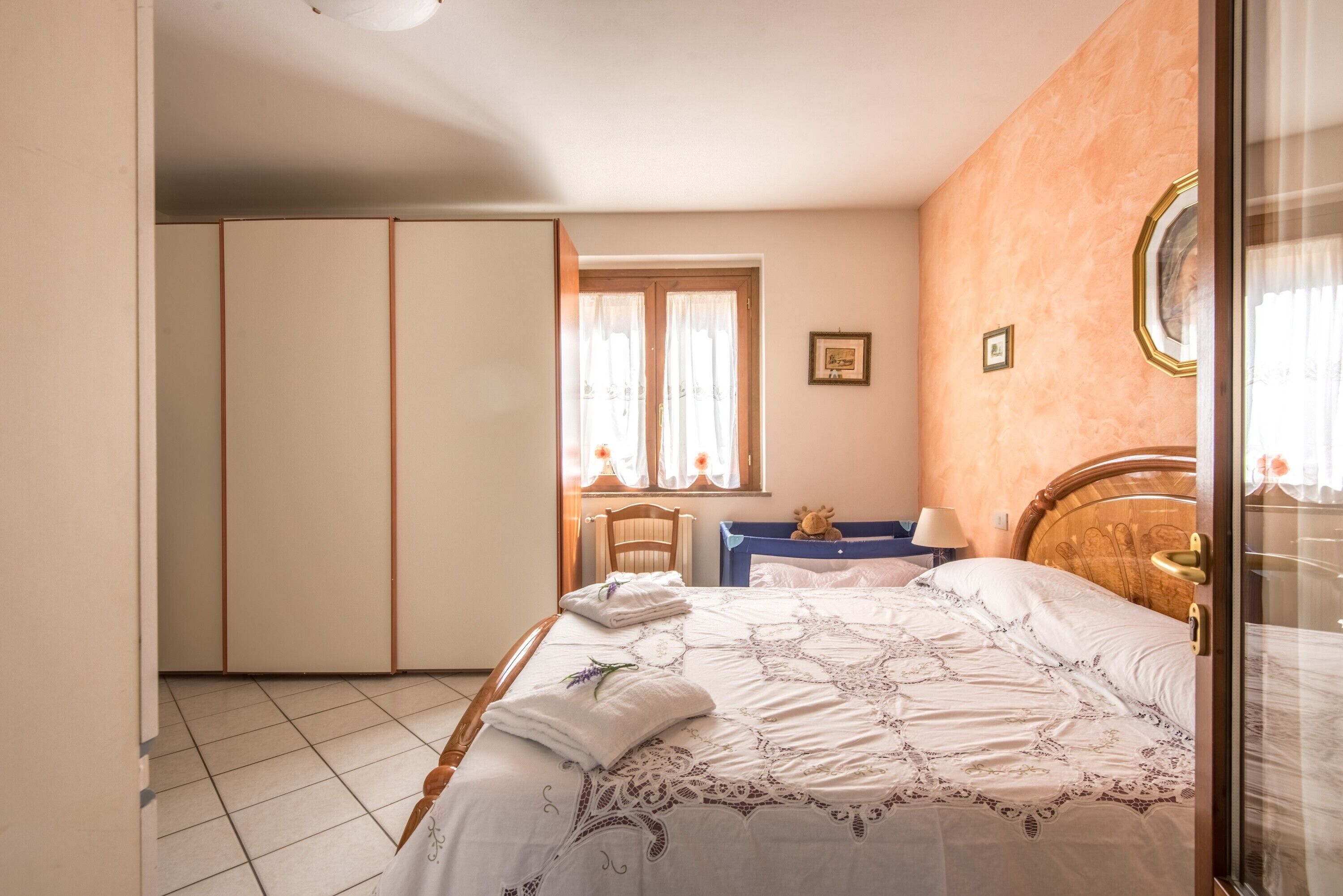 Un dormitorio con cama, armario, ventana con cortinas y mesita de noche.