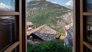Vista sulle montagne attraverso una finestra, con edifici in pietra e cielo sereno.
