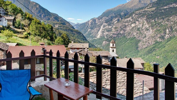 Vista sulle montagne con un patio in legno, un tavolo e una sedia.