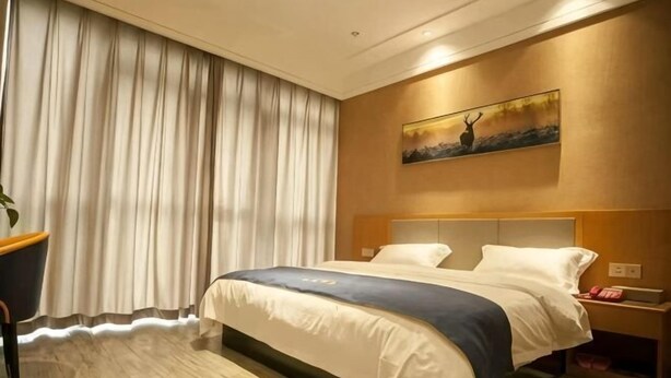 Una habitación de hotel con una cama grande, cabecera, un cuadro en la pared y una cortina.