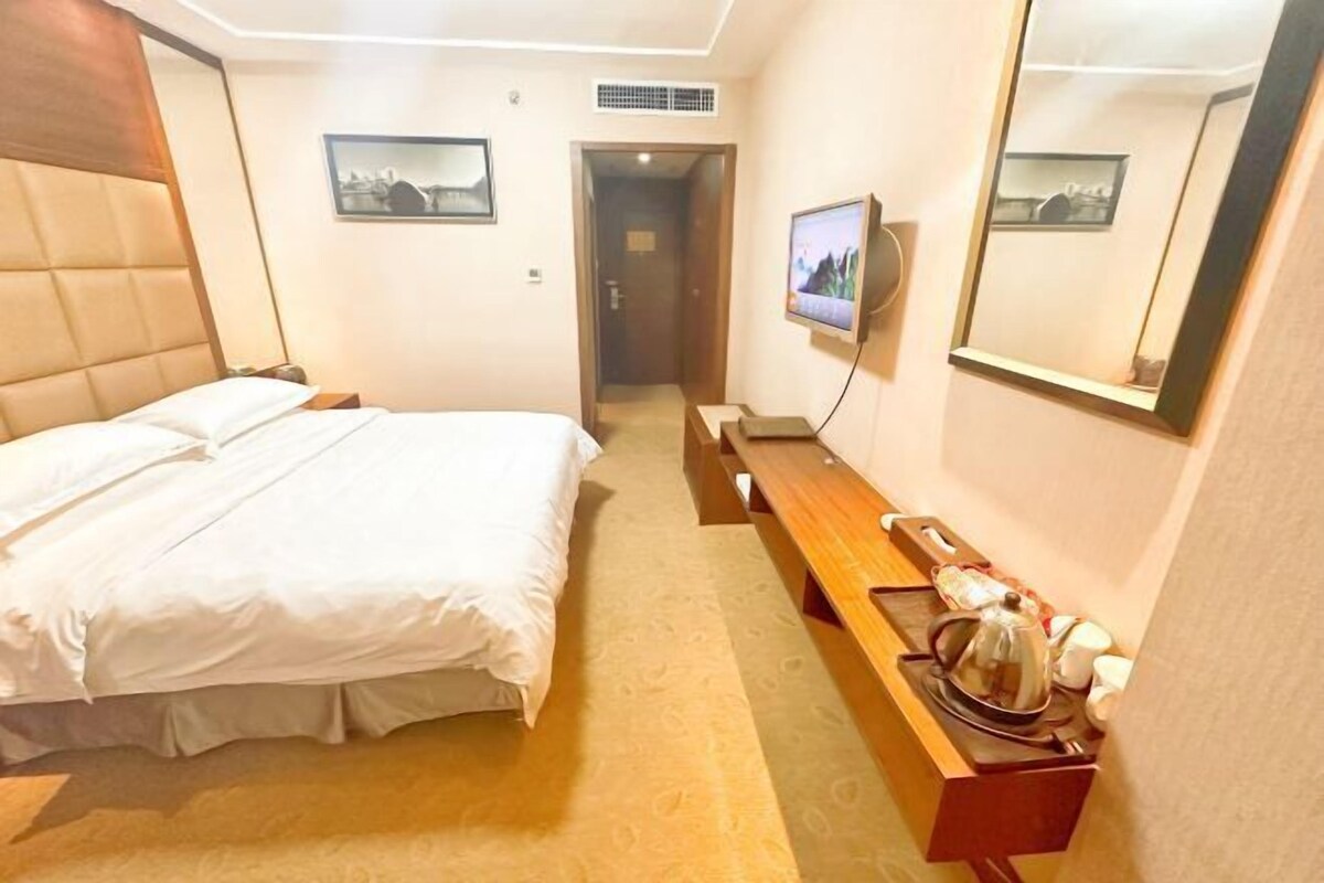 A hotel room with a large bed, a wooden bench, a TV, and a mirror.