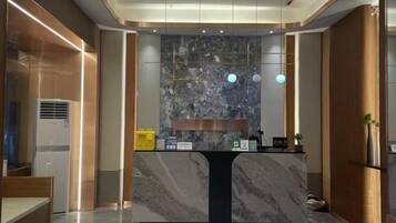 A reception desk with a marble top, a wall-mounted clock, and a small plant on the right.