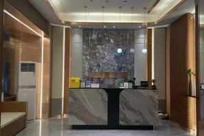 A reception desk with a marble top, a wall-mounted clock, and a small plant on the right. - Hailian Xianggan Hotel (Yongxin)