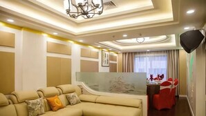 Una habitación de hotel moderna con un sofá seccional beige grande, un área de comedor con sillas rojas y un espejo grande.