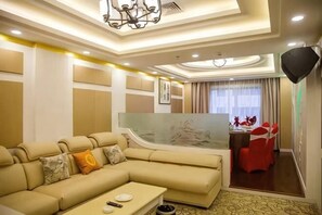 Une chambre d’hôtel moderne avec un grand canapé d’angle beige, un coin repas avec des chaises rouges et un grand miroir.