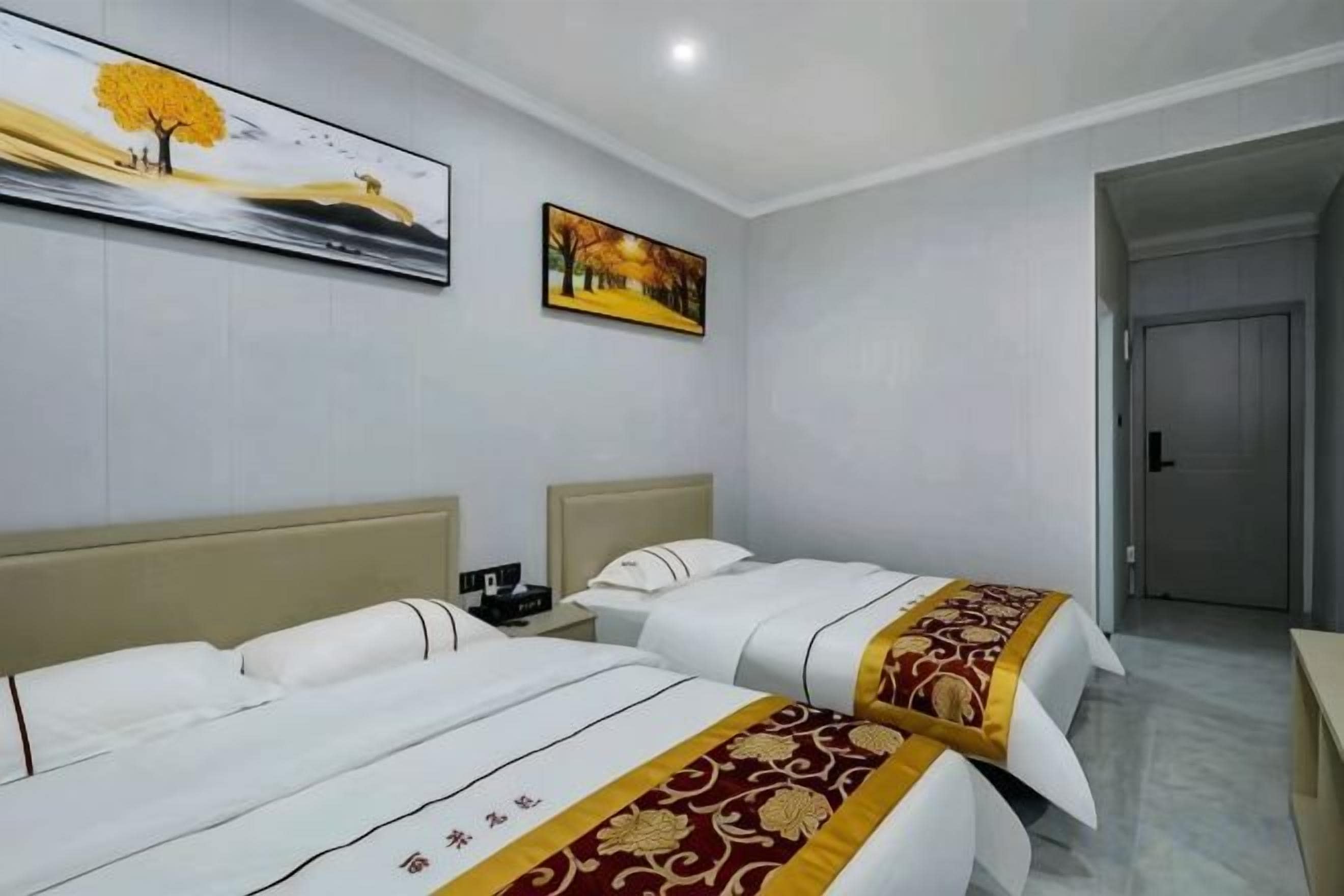 A hotel room with two beds, a painting on the wall, and a door to the right.