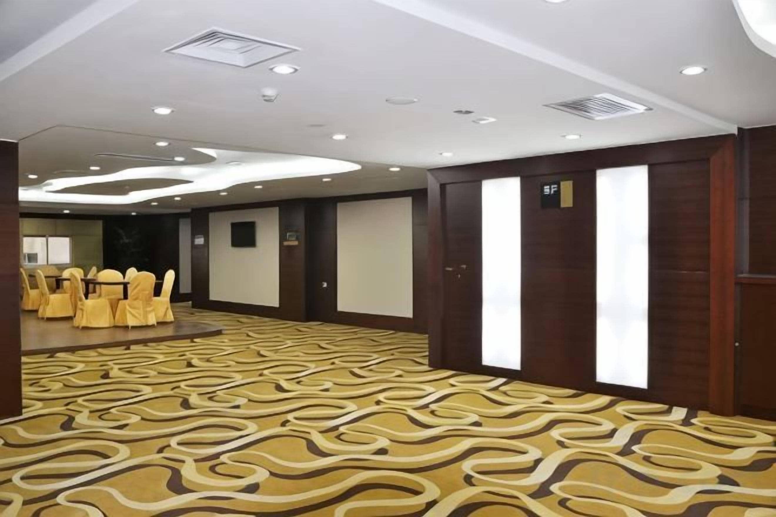A conference room with a patterned carpet, round tables with chairs, and a large screen.